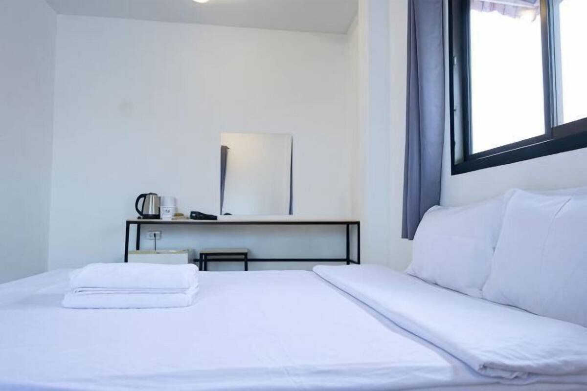 Ett hotellrum med en säng, ett skrivbord med en stol, en spegel och ett fönster med gardiner.