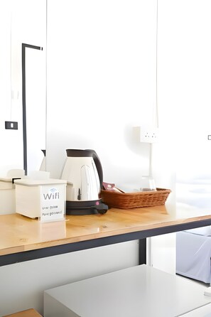 Een nette, moderne hotelkamer met een houten bureau, een mand, een waterkoker en een bordje met informatie over WiFi.