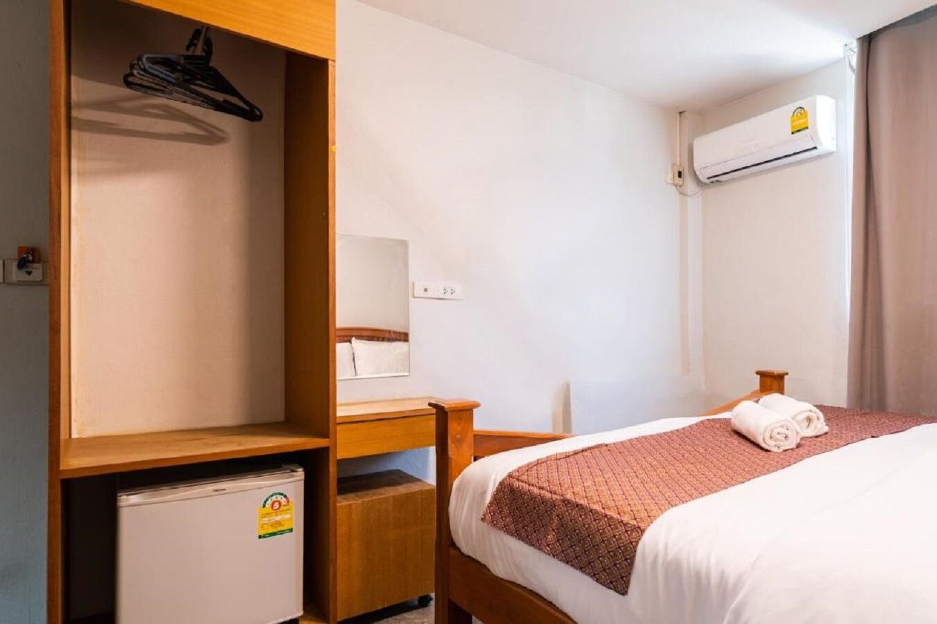 Habitació d'hotel amb llit, armari de fusta, escriptori, nevera petita, mirall i aire condicionat.