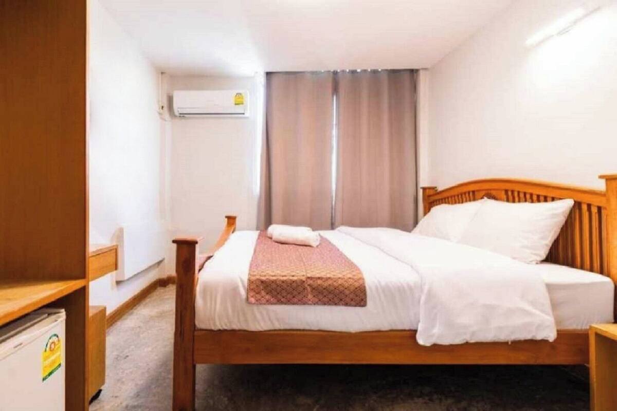Un lit simple avec une tête de lit en bois, une table de chevet, un petit bureau et un appareil de climatisation fixé au mur.