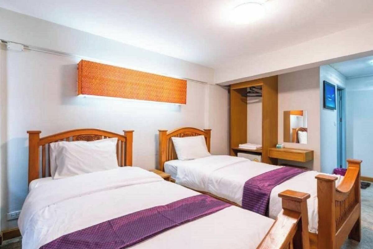 Une chambre d’hôtel avec deux lits en bois, une petite table de chevet, un miroir et une étagère fixée au mur.