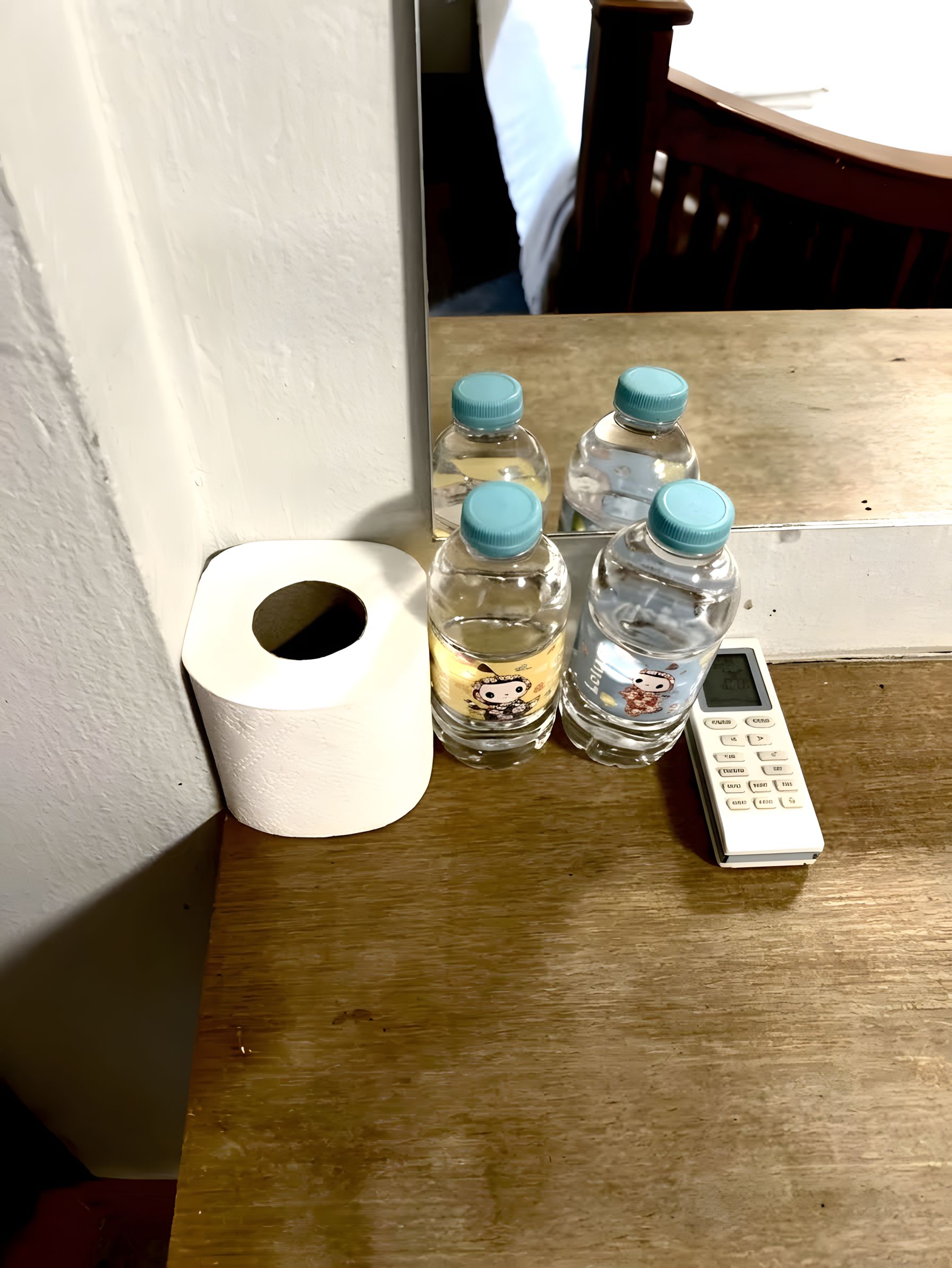 Ein Holztisch mit einer Toilettenpapierrolle, zwei Wasserflaschen und einer Fernbedienung.