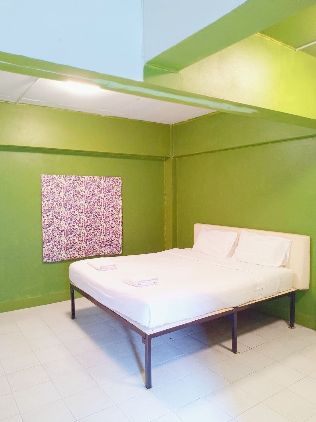 Una habitació amb parets verdes, un llit blanc i un tapís floral a la paret.