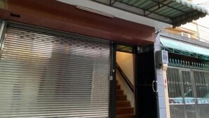 Un edificio con una persiana baja, una escalera que sube a un piso superior y una entrada protegida por una reja.