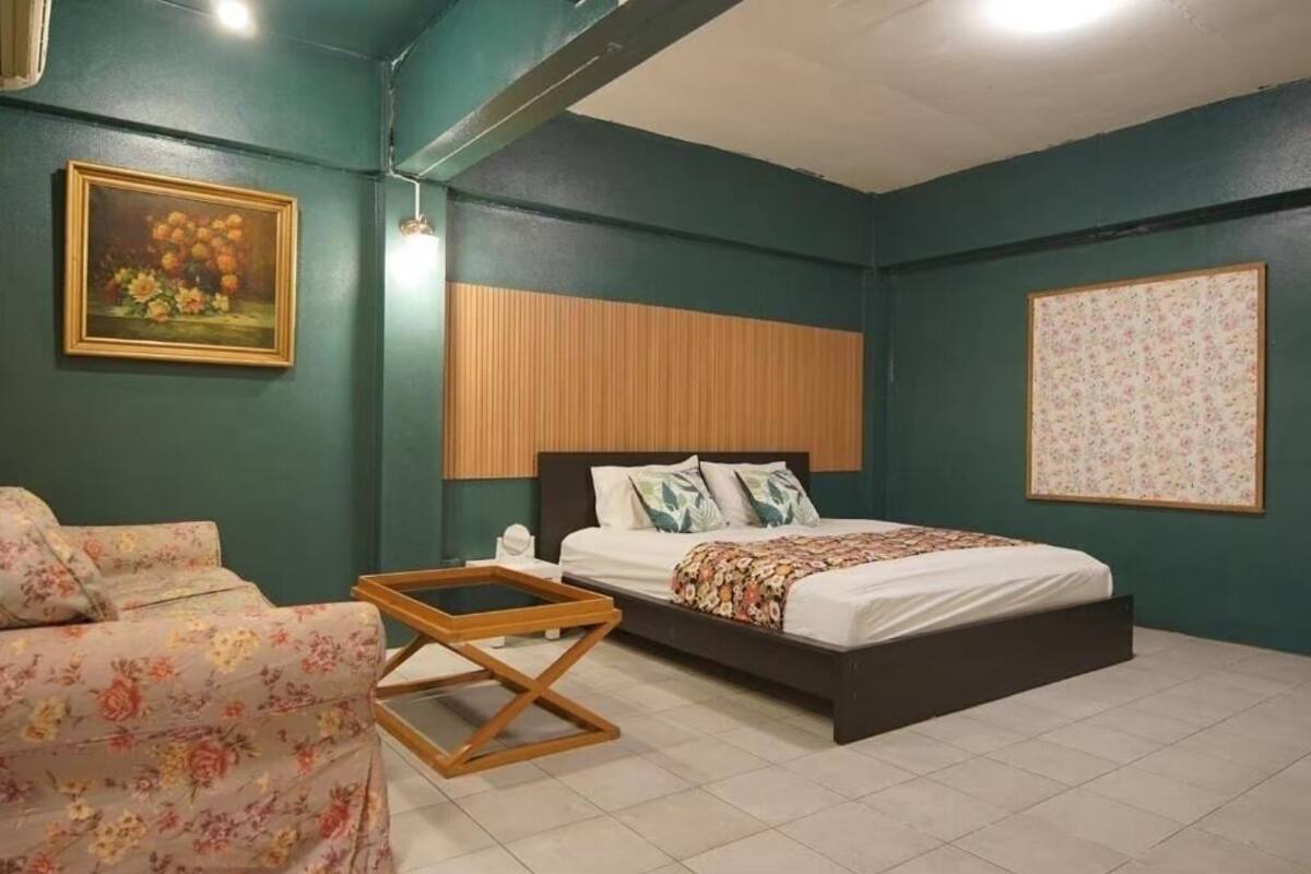 Een slaapkamer met een bed, een houten hoofdbord, een bank met bloemenprint en een kleine tafel.