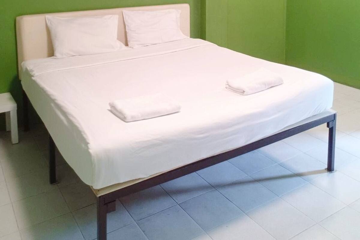 Een opgemaakt bed met witte lakens en kussens in een kamer met groene wanden en een wit plafond.