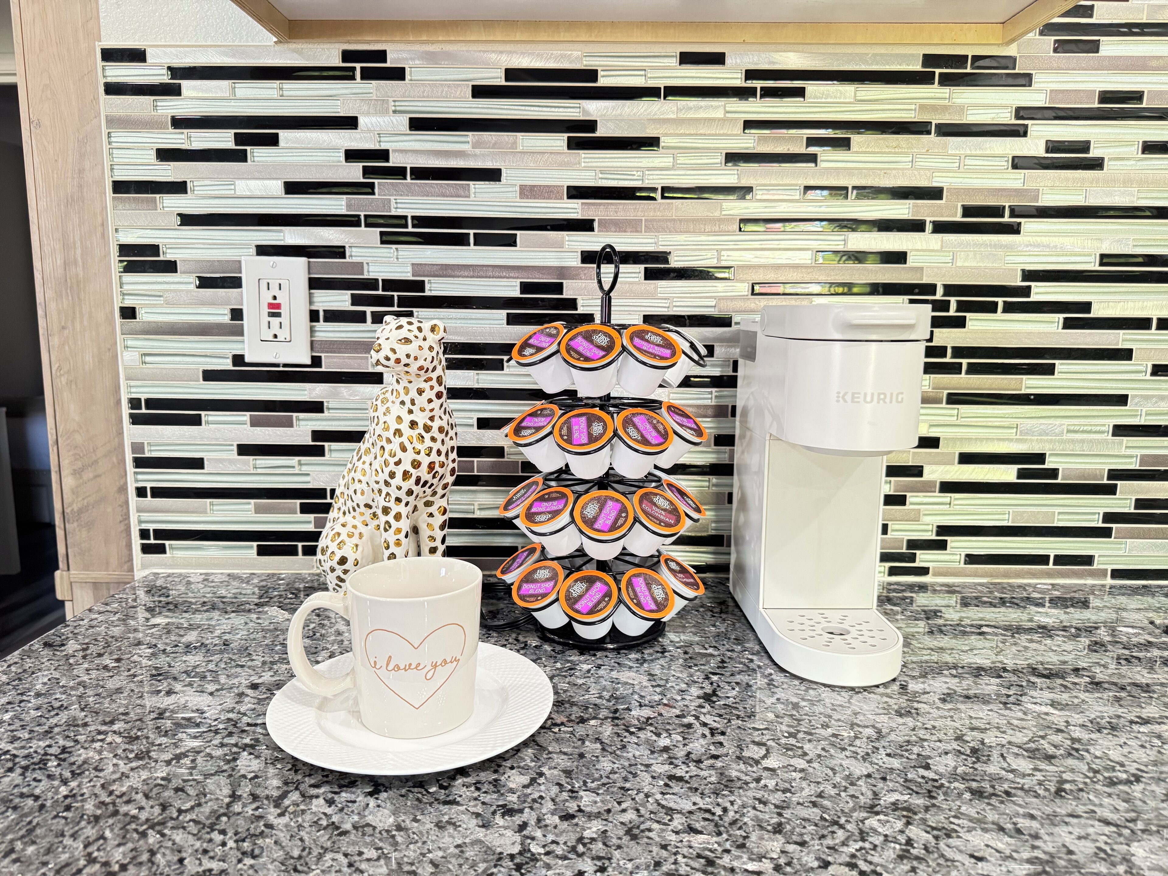 A kitchen counter with a coffee maker, a mug with a heart design, and a mug holder with multiple cups.
