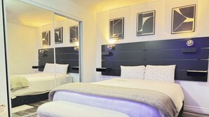 Een moderne slaapkamer met een groot bed, een bankje, een garderobe en kunst aan de muur.
