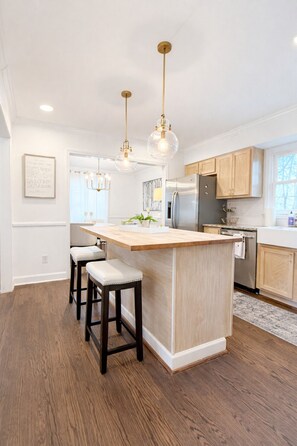 A modern kitchen with a central island, bar stools, pendant lighting, and wooden cabinetry. - BBQ • Swingset • Pets OK • Family Retreat (Charlotte)