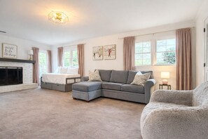 A spacious living room with a fireplace, a grey sectional sofa, a grey armchair, and a bed with a white headboard. - BBQ • Swingset • Pets OK • Family Retreat (Charlotte)