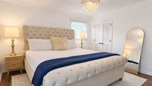 A bedroom with a large bed, two bedside tables, a chandelier, a window, and a mirror. - BBQ • Swingset • Pets OK • Family Retreat (Charlotte)