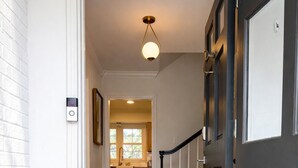 A hallway with a wooden floor, a black and white striped doormat, and a door with a black frame. - BBQ • Swingset • Pets OK • Family Retreat (Charlotte)
