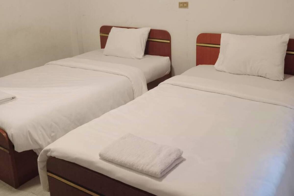 Una habitación con dos camas individuales, cada una con cabecero de madera y ropa de cama blanca.