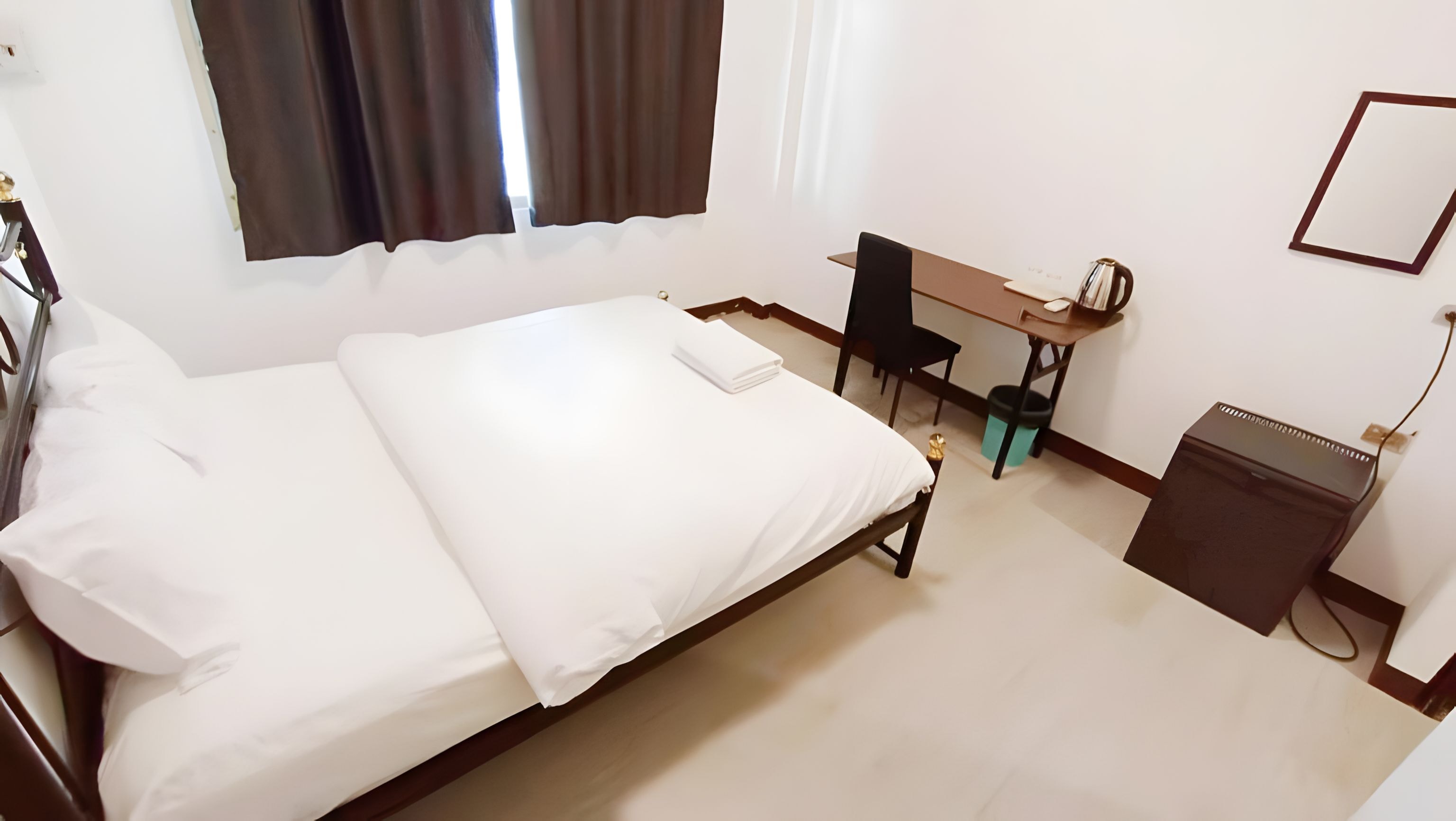 Una habitación de hotel con una cama, un escritorio, una silla y un pequeño armario.