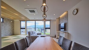 Una sala de conferencias moderna con una larga mesa y asientos cómodos, ventanas amplias con vistas a la ciudad y un televisor montado en la pared.