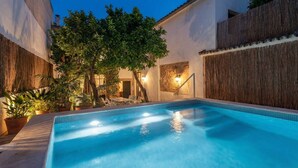 Una piscina rectangular con agua azul cristalina, rodeada por una valla de madera, plantas en macetas y un muro de piedra.