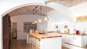 Una cocina moderna con una isla central, taburetes de madera, iluminación colgante y un techo rústico.