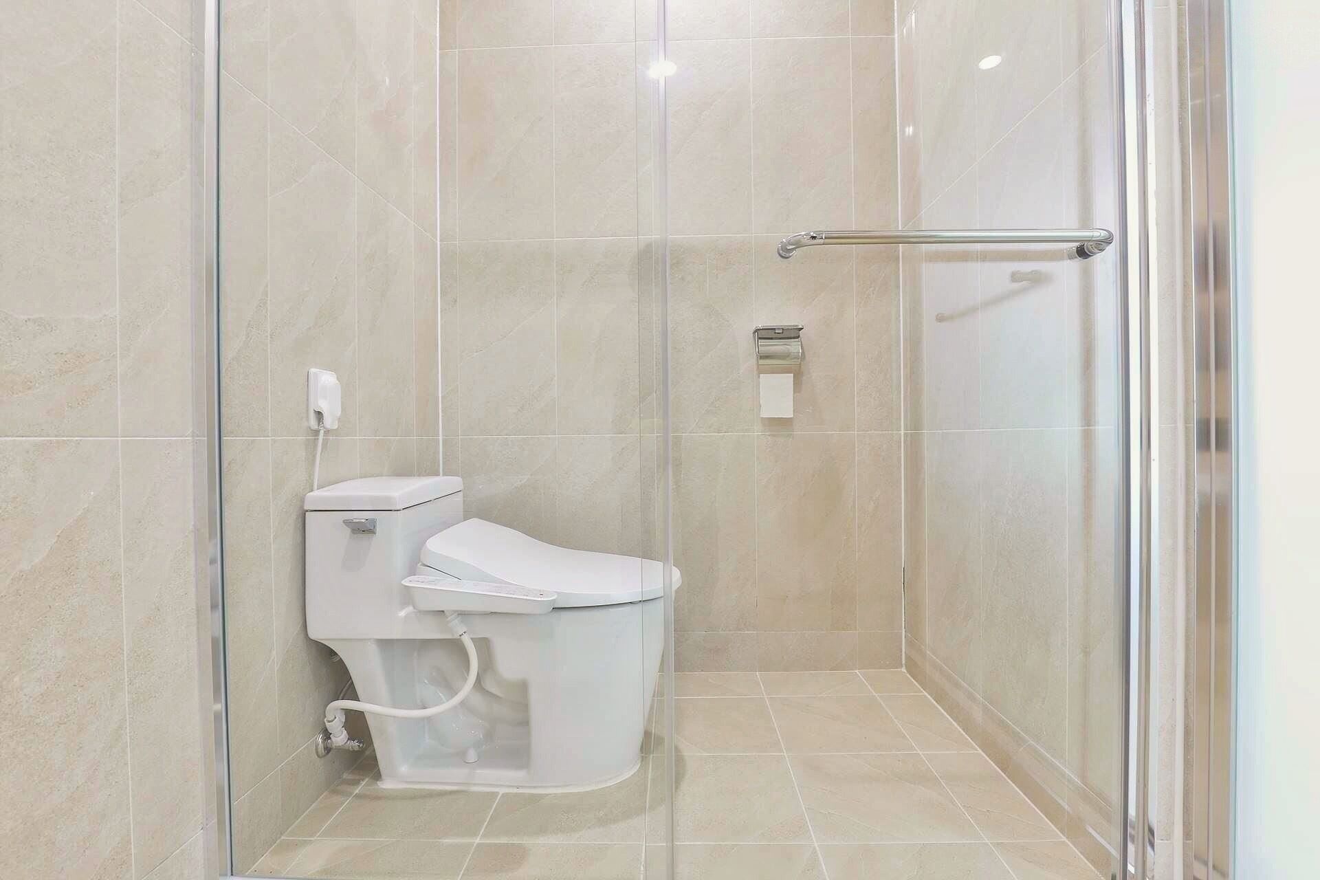A modern bathroom with a glass shower enclosure, a toilet, and a hand dryer.