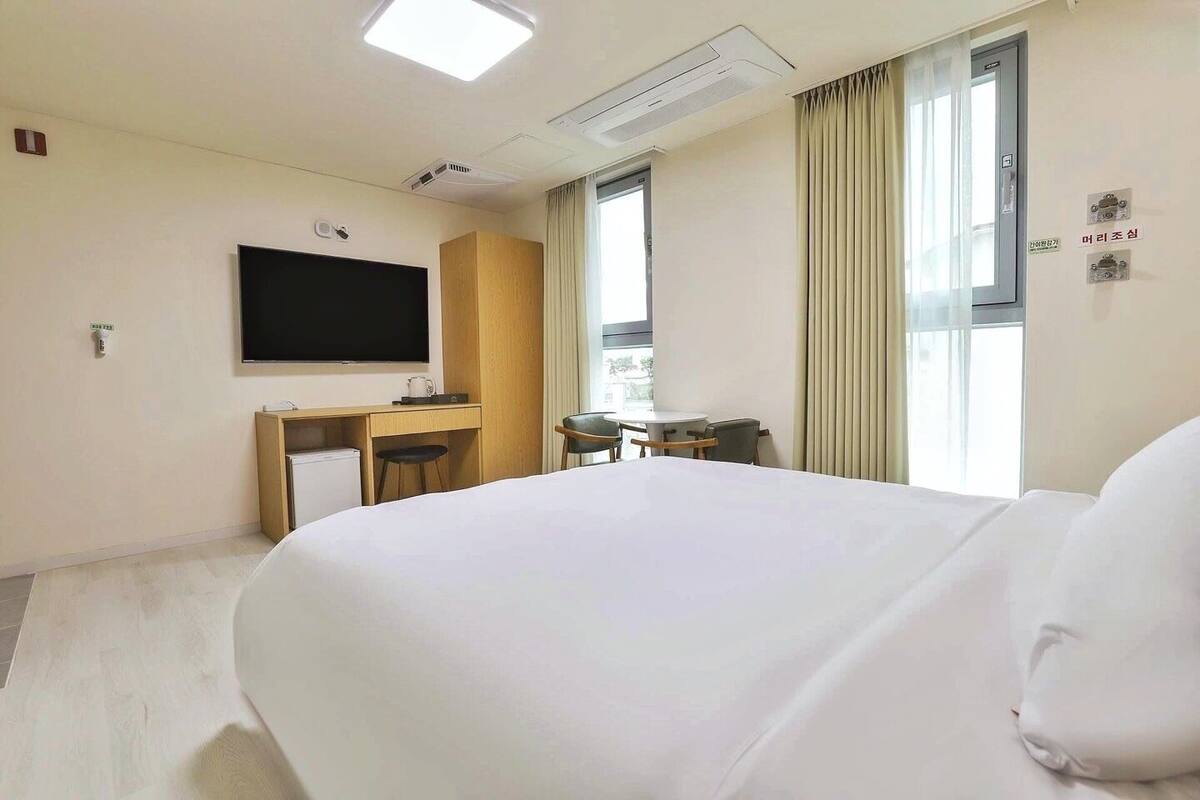 A hotel room with a large bed, a desk, a chair, a television, and a window with curtains.