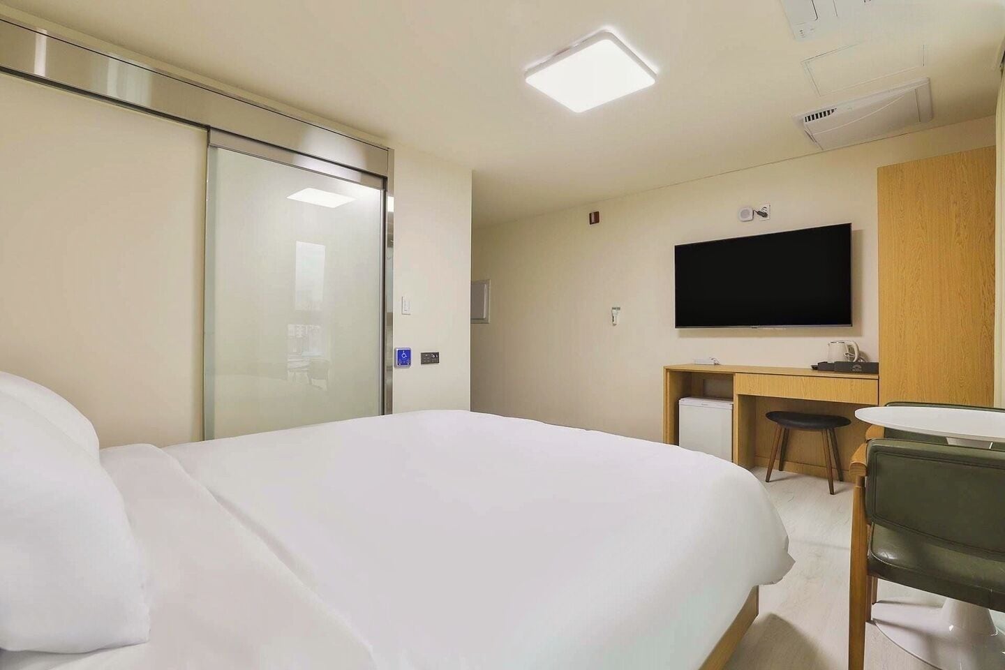 Habitación de hotel con cama, escritorio, silla, televisor y una pequeña kitchenette.