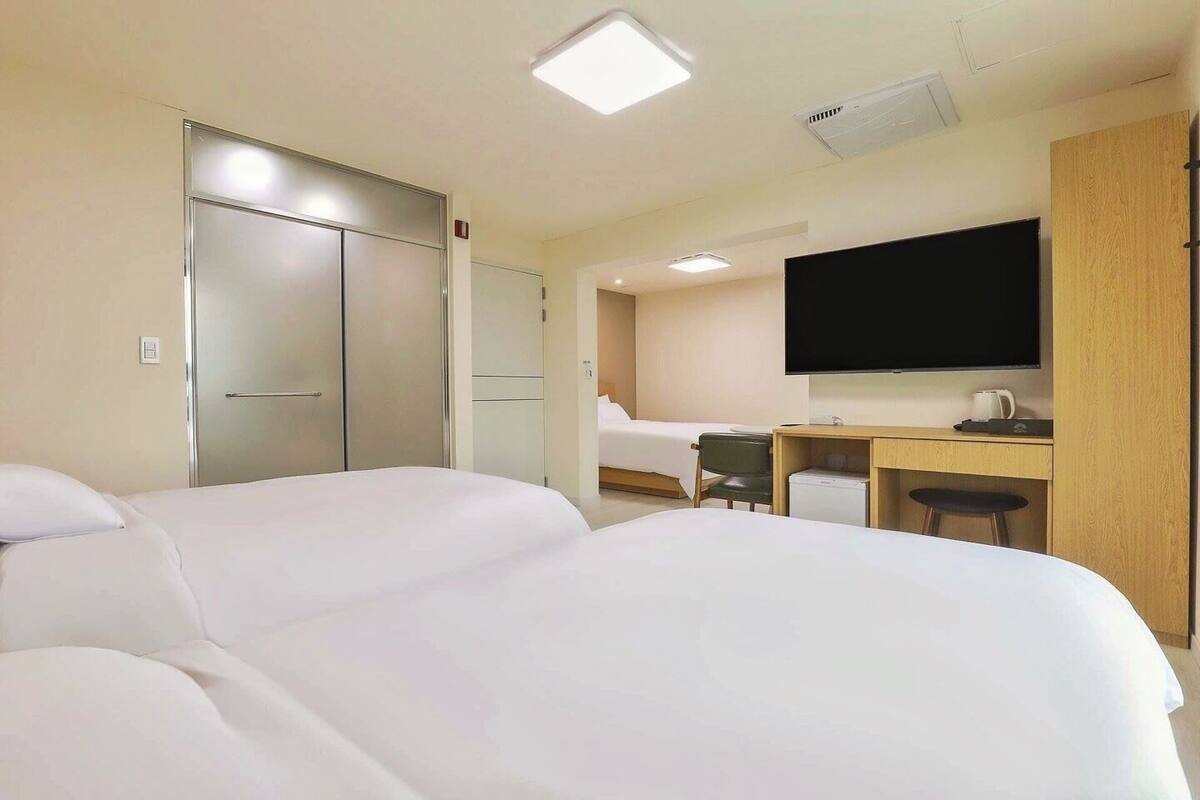 A hotel room with two beds, a desk, a chair, a television, and a wardrobe.