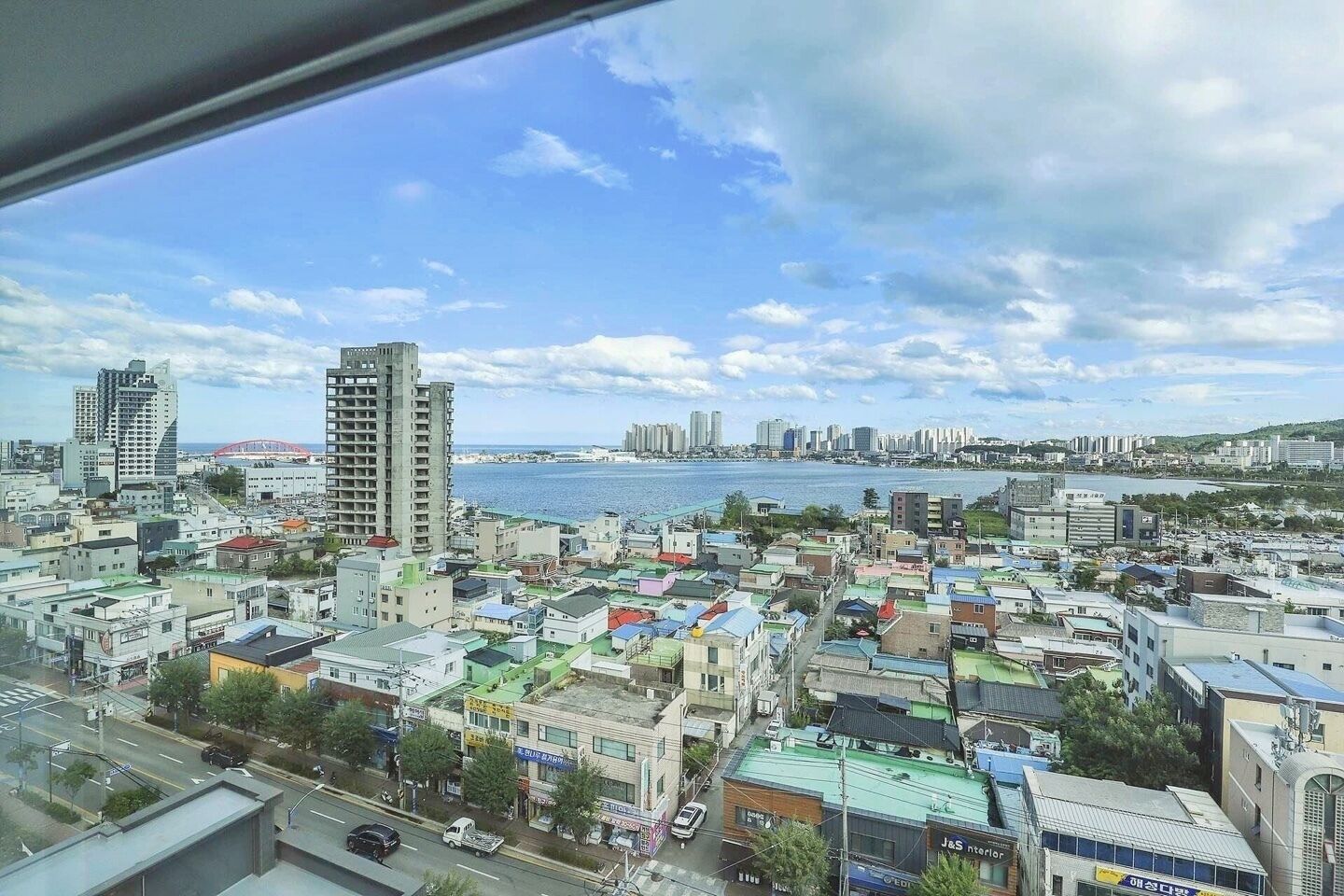 A coastal cityscape with a mix of residential and commercial buildings, a prominent waterfront, and a view of the sea.