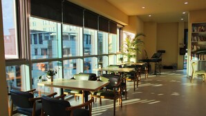 A spacious indoor area with large windows, wooden tables and chairs, a piano, and a bookshelf. - Hotel BERITH (Sokcho)