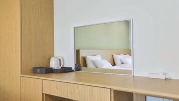 A hotel room with a wooden desk, a coffee maker, a remote control, and a bed with white pillows.