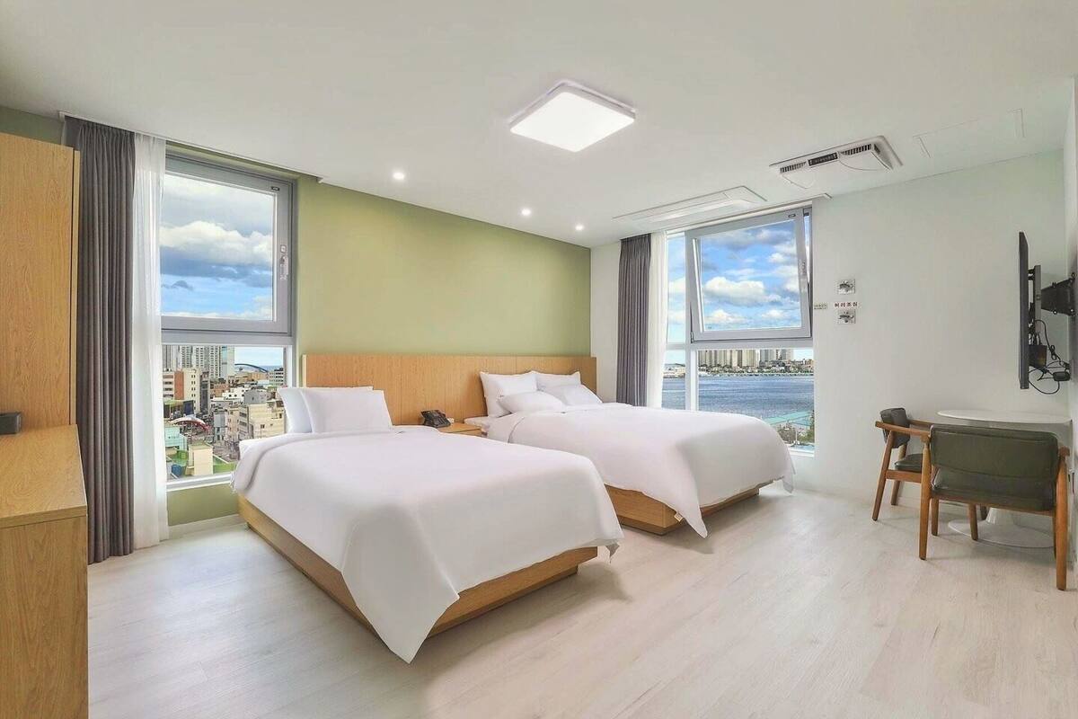 A hotel room with two beds, a desk, and a view of a cityscape.