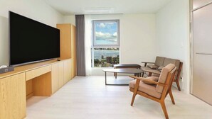 A modern living room with a flat-screen TV, wooden furniture, a view of the city through large windows, and a balcony. - Hotel BERITH (Sokcho)
