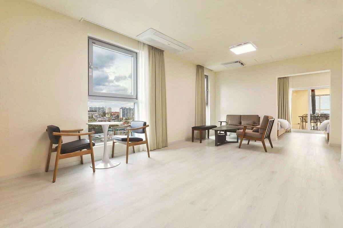 A spacious living room with a large window, a sofa, a dining table, and two chairs.