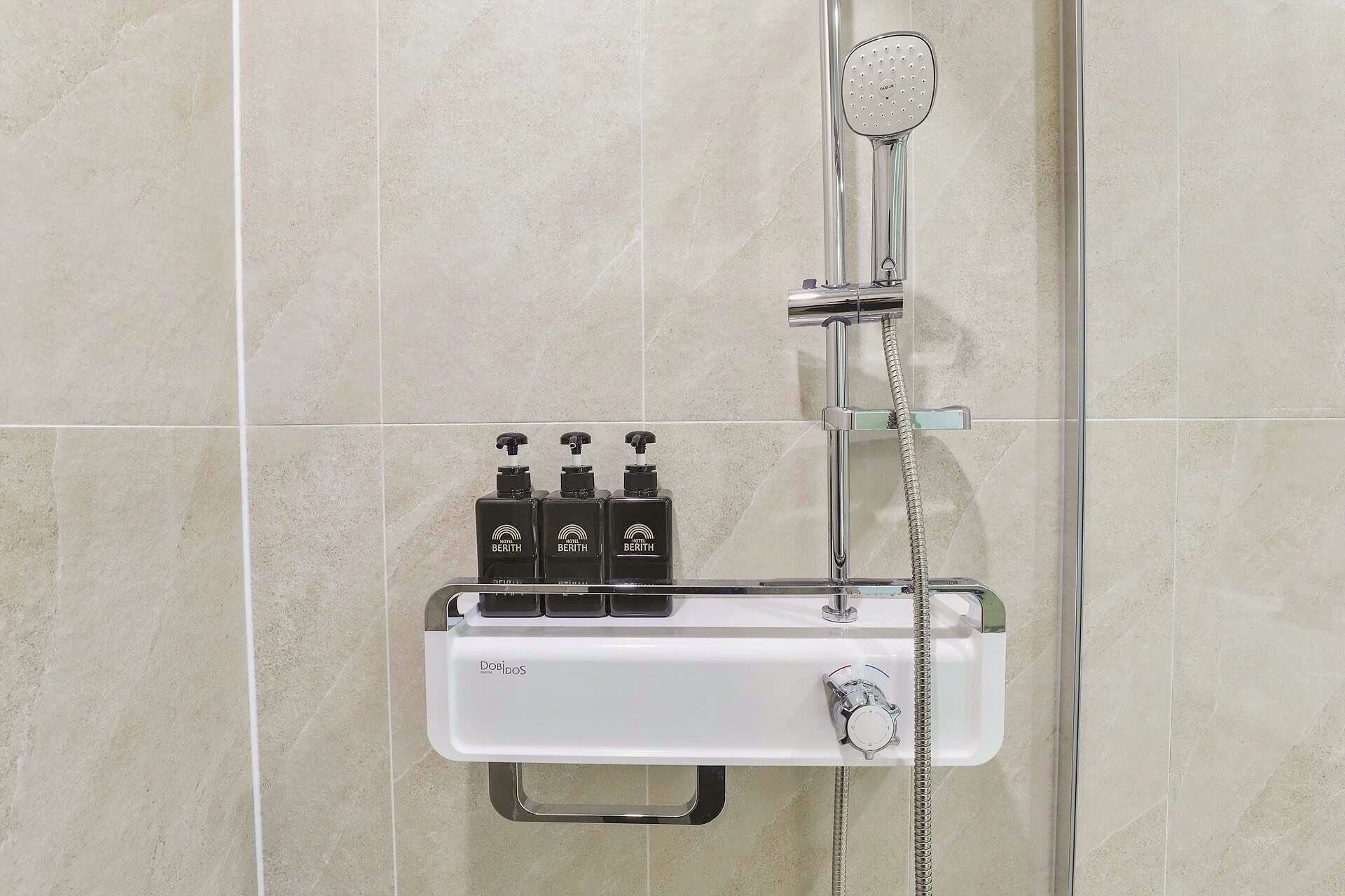 A shower with a handheld showerhead, a handheld soap dispenser, and a soap dish.