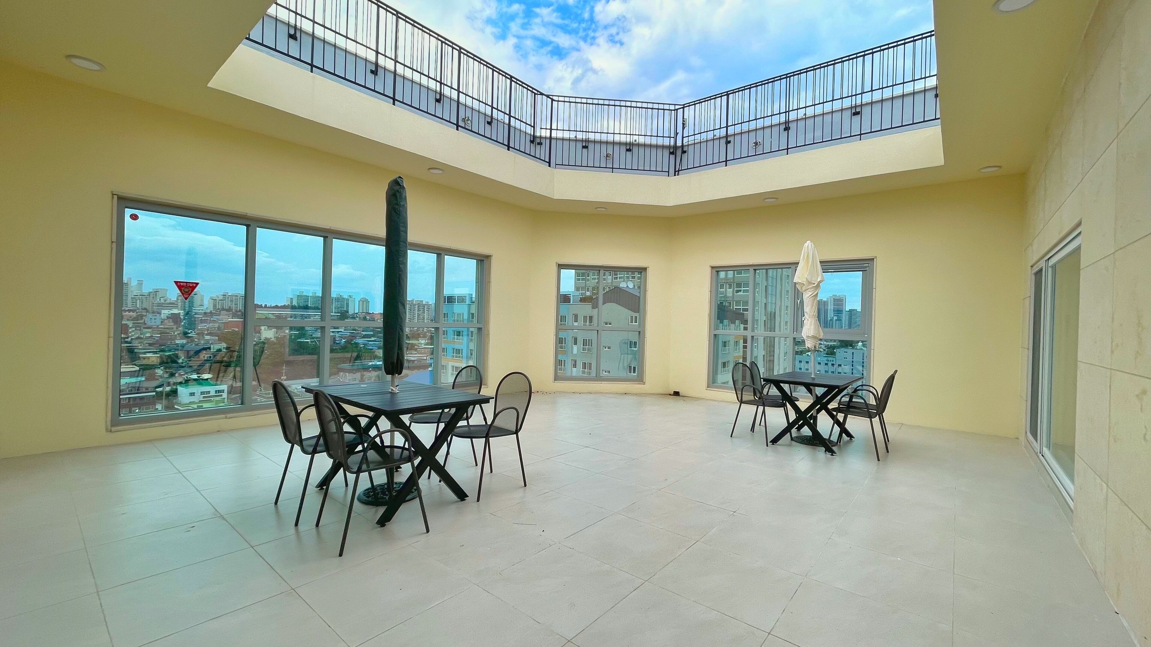 Ein geräumiger Balkon mit geschwungener Reling, große Fenster mit Blick auf die Stadt und eine Essecke mit Tisch und Stühlen.
