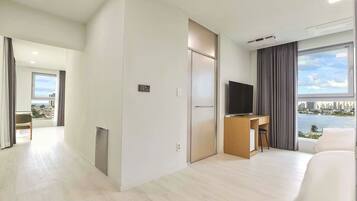 A modern hotel room with a city view, a desk with a chair, a television, and a large bed.