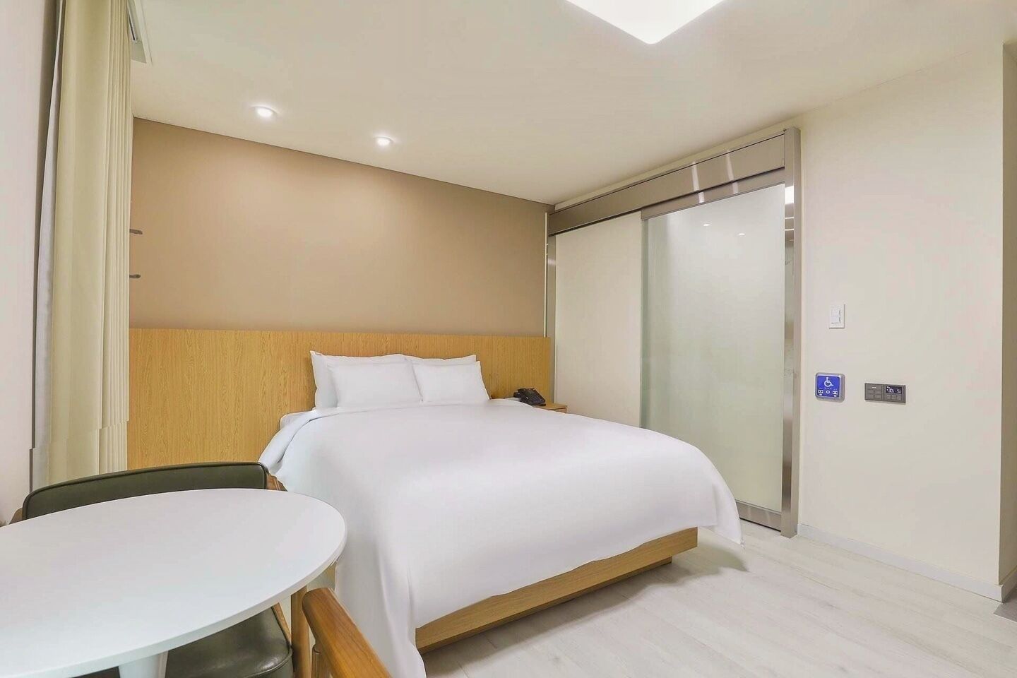 A hotel room with a bed, a bedside table, a chair, a wardrobe, and a bathroom door.