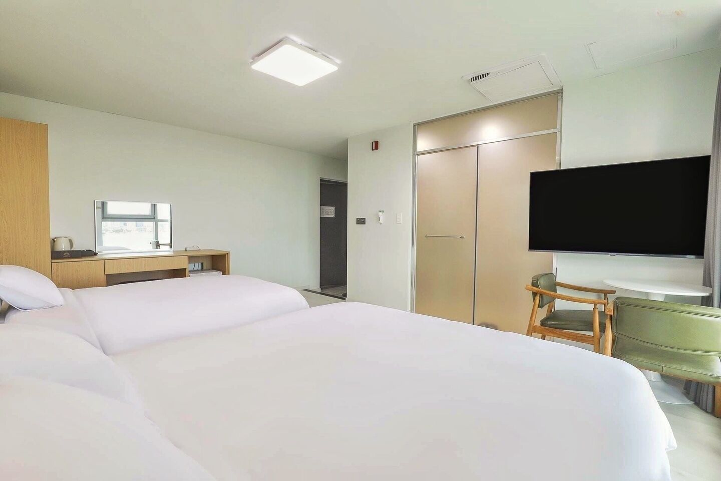 Une chambre d’hôtel avec deux lits, un bureau avec une chaise, une télévision et une armoire.
