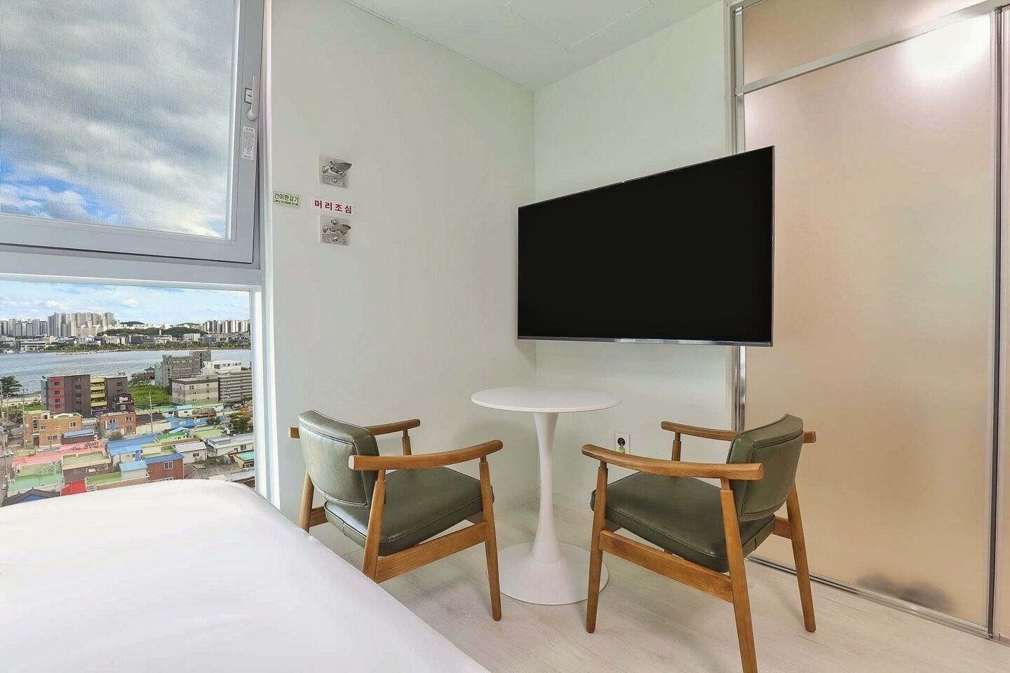 A hotel room with a bed, two chairs, a small table, a TV, and a view of a cityscape.