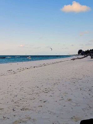 A beach with a sandy shore, calm sea, and a few boats.