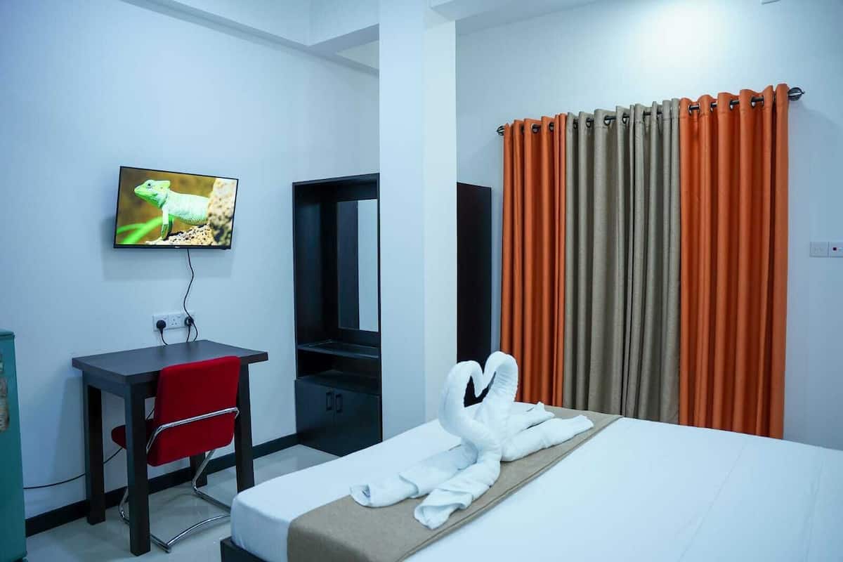 A hotel room with a bed, a desk, a chair, a TV, and a window with curtains.