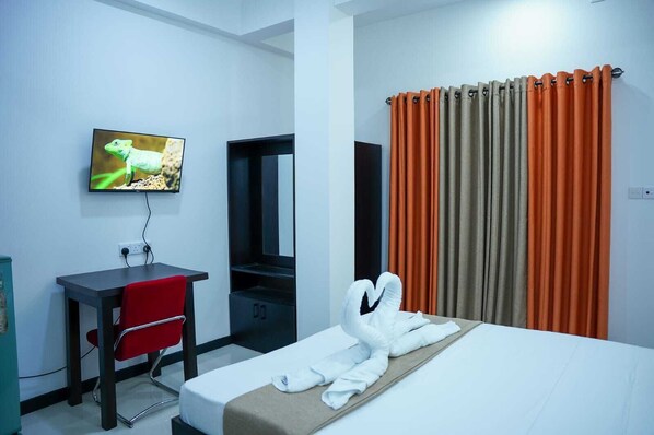 A hotel room with a bed, a desk, a chair, a TV, and a window with curtains.