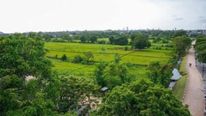Paisaje rural con campos verdes, un curso de agua y un sendero con dos personas caminando.