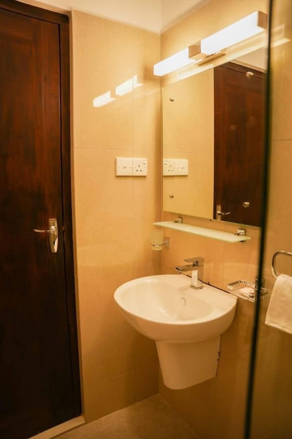 Une salle de bain avec une porte en bois, un lavabo blanc, un miroir et un luminaire placé au-dessus du miroir.