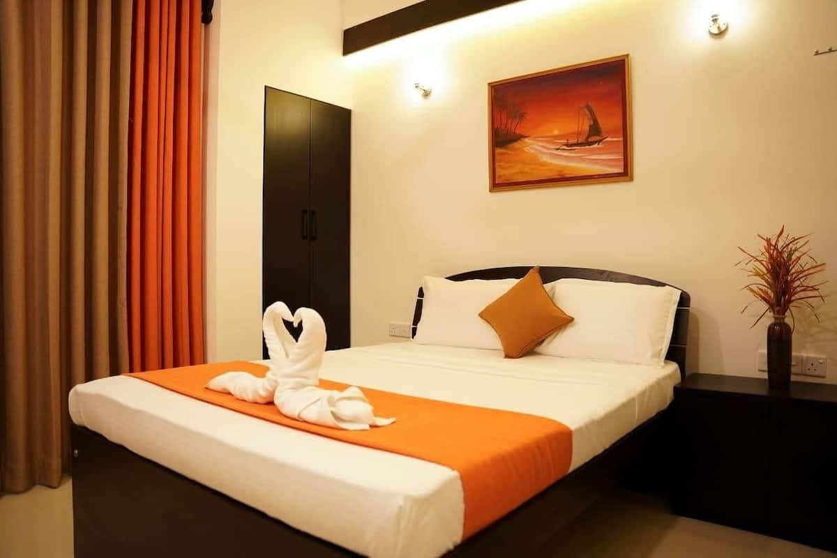 A hotel room with a bed, a painting, a vase with plants, and a door.