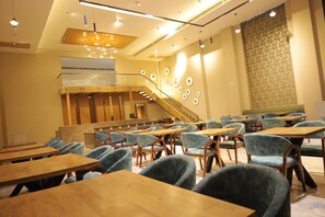 A conference room with multiple tables and chairs, a staircase, and a patterned wall. - Clarks Inn Etawah (Etawah)