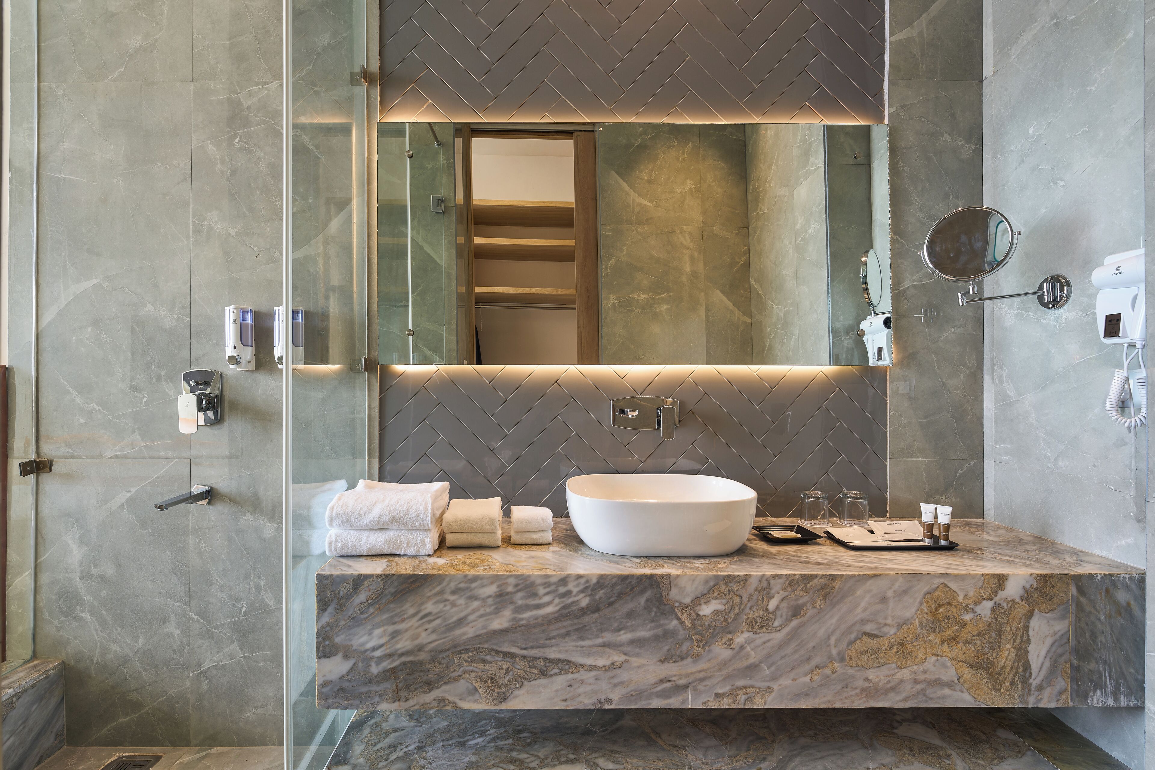 A modern bathroom with a large mirror, a white vessel sink, and marble countertops.