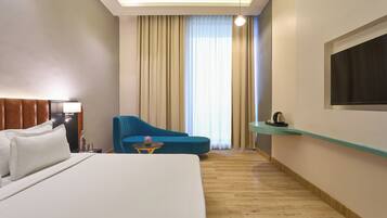 A hotel room with a large bed, a blue armchair, a small table with a lamp, and a TV mounted on the wall.