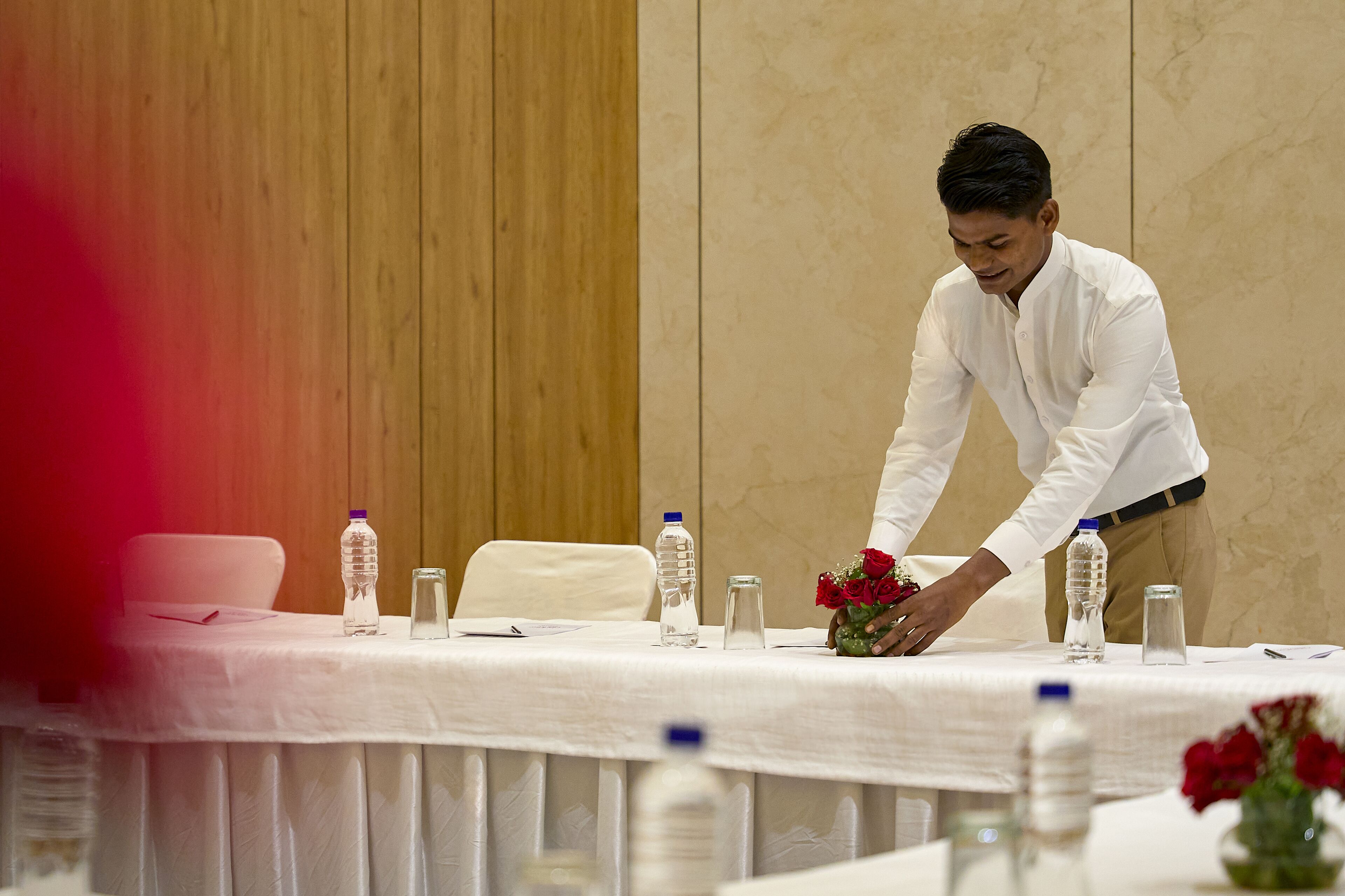 Una mesa de conferencias con botellas de agua, un florero con rosas rojas y un bolígrafo.