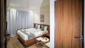 A hotel room with a bed, a small table, a chair, a TV, and a wooden door. - Sunbright Rooms Residency Hotel  (Thane)