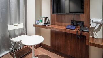 Zona de recepción de hotel con mostrador de madera, televisor de pantalla plana, teléfono y silla plegable.