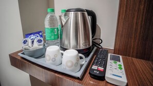 A tray with a kettle, two cups, two bottles of water, a pack of tissues, and a remote control on a wooden surface. - Sunbright Rooms Residency Hotel  (Thane)